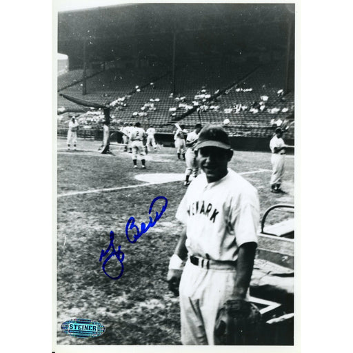 Yogi Berra Signed B/W 5x7 Photo (Standing on Field w/Team warming up in Background)